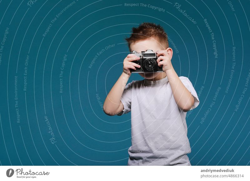 Little boy taking a picture using a retro camera. Child boy with vintage photo camera isolated on blue background. Old technology concept with copy space. Child learning photography