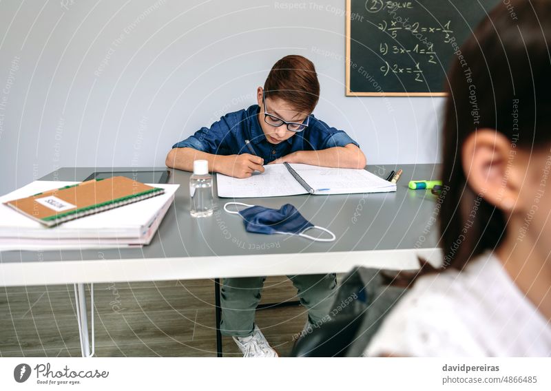 Boy writing in his notebook at school child student classroom mask on desk covid-19 safety hand sanitizer virus copy space people epidemic education no mask