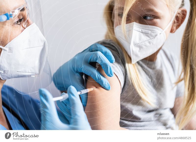 Little girl in face mask in doctor's office get vaccinated. Syringe with vaccine for covid-19 coronavirus, flu, dangerous infectious diseases. Injection after clinical trials for human, child.