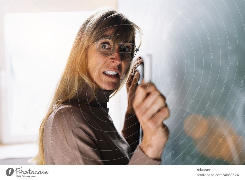 Angry teacher in glasses with Chalk in hand in front of a blackboard angry stick crazy grudge grouch professor school person woman adult background chalkboard