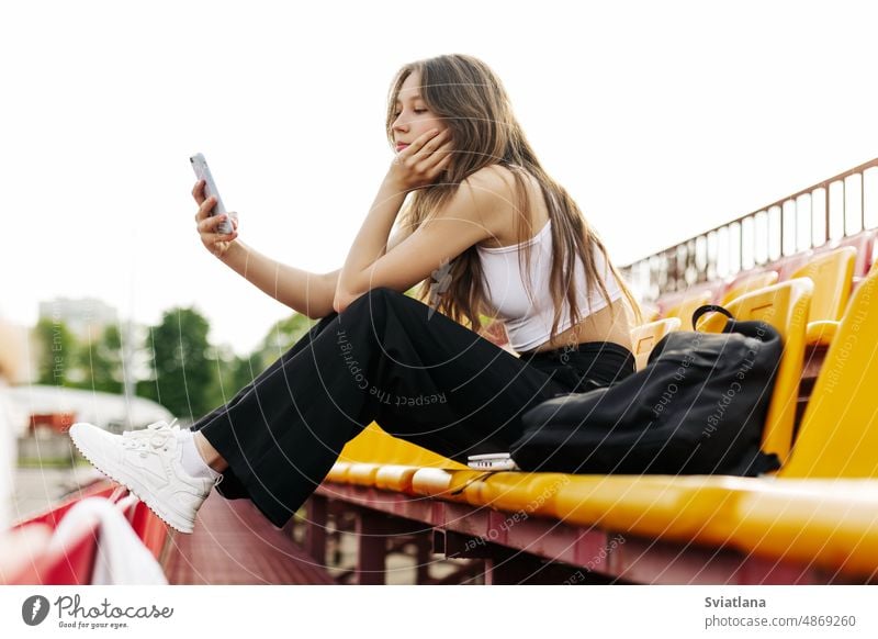 A teenage girl sits on the school bleachers and writes a message on her phone in her free time schoolgirl daytime smartphone stadium texting education sitting