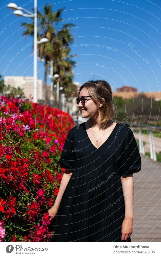 Young female tourist admiring the view of European city on sunny day. Woman sightseeing in summer on vacation. Heatwave in Europe affecting tourists and travelers. Red flowers blooming in the city.