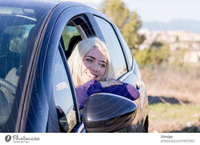 Smiling young woman looks out of a car window journey arms crossed person vacation travel leaning adult happy transport smiling female portrait outdoors