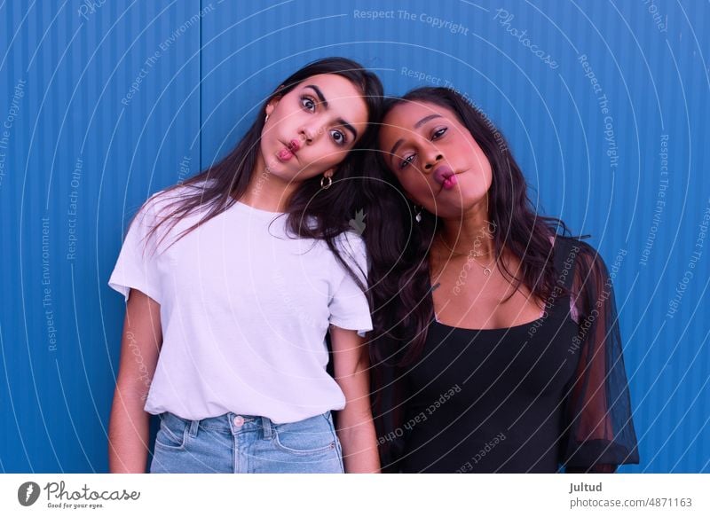 Two friends of different ethnicity listen to music in front of a blue wall. Girl Ethnicity spain Young Woman Twenties Trendy BuildingExterior Girlfriend