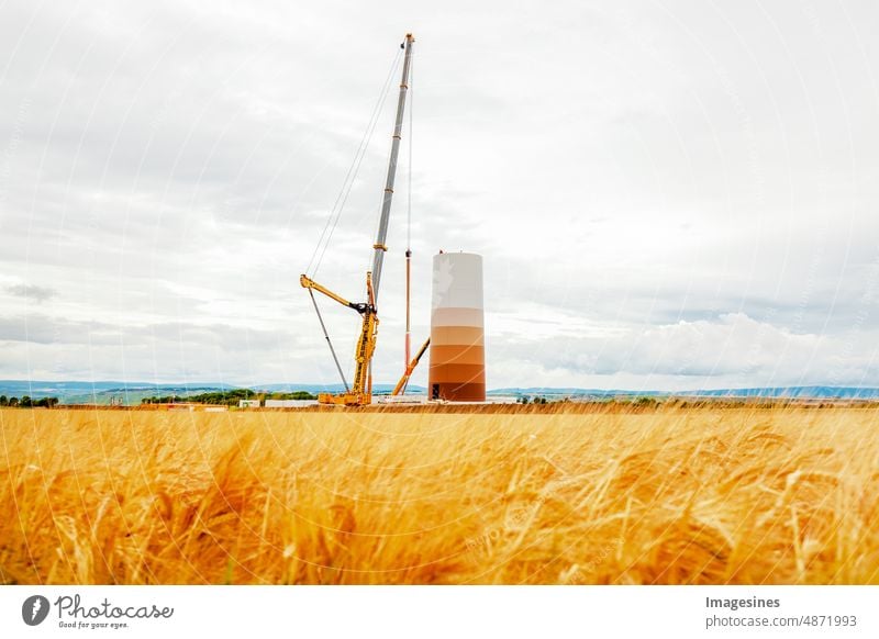 Construction and assembly of a wind turbine by crane on a construction site. Farmland with construction work on wind farm in Germany. Energy saving concept from wind turbine construction with cloud sky