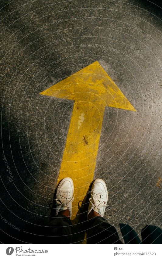 A person stands in front of a directional yellow arrow Arrow Direction groundbreaking Navigation Target Orientation Road marking onwards Future Human being