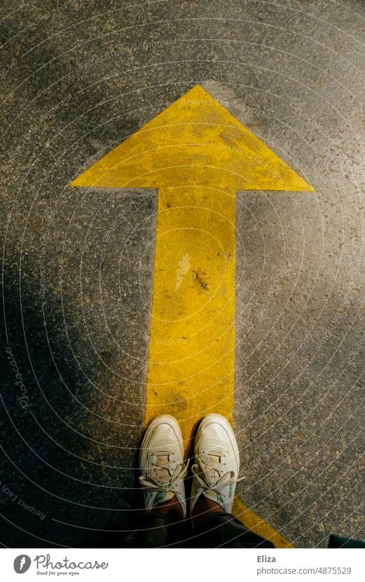 A person stands in front of a directional yellow arrow Arrow Direction groundbreaking Navigation Target Orientation Road marking onwards Future Human being