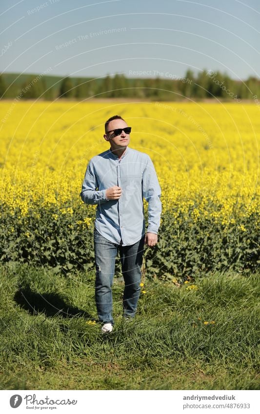 A young man in sunglasses is walking and having fun through a Sunny yellow rapeseed field, the concept of travel and freedom. summer holiday background people