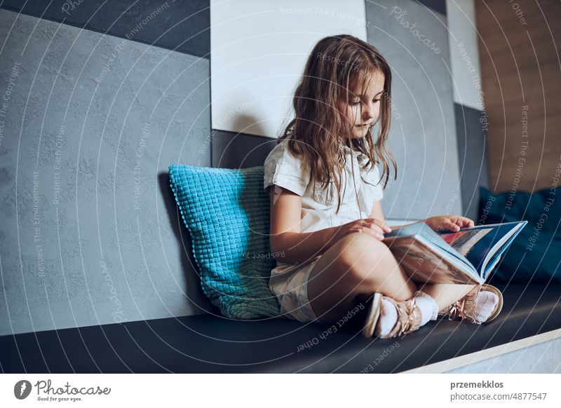 Schoolgirl reading book in school library. Primary school pupil is engaged in book. Child doing homework. Smart girl learning from book. Child curiosity back