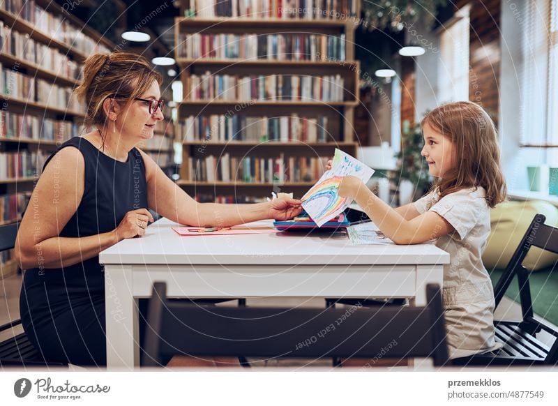 Teacher assisting schoolgirl during art class looking at child drawing. Child doing homework sitting at desk in afterschool club. Learning at primary school. Elementary education. Back to school