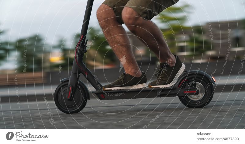 Close up of man riding black electric kick scooter at cityscape at night with motion blur e-scooter downtown sneakers bike drive activity traffic electrically