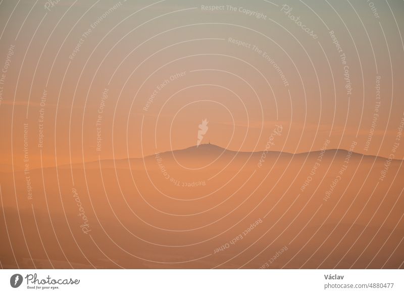 Frosty and foggy morning on the Polish Ochodzita mountain with a view of the Czech Beskydy mountains. Lysa mountain illuminated with orange light. Winter and frosty environment