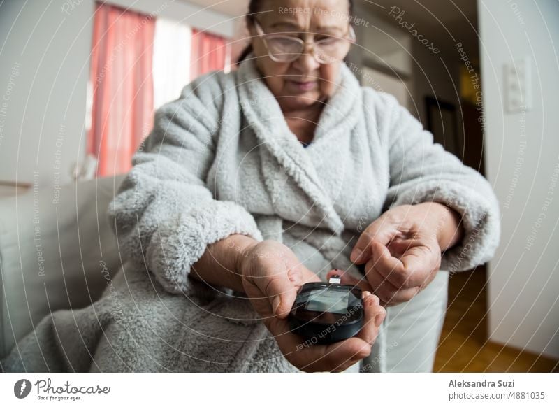 Senior woman checking blood sugar level using home glucometer. Old person with diabetes at home in living room.. Diabetes treatment for elderly people.