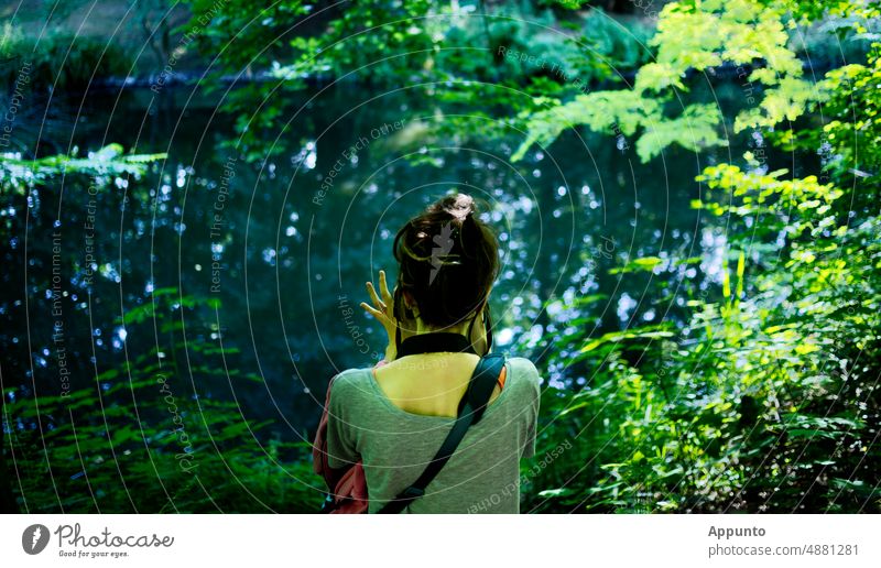 A young woman sits on the shore of a lake, ... observes and photographs nature Take a photo take pictures Nature Lake in the country Light Green hobby