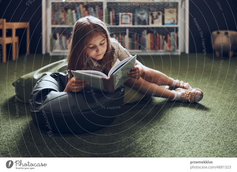 Schoolgirl reading book in school library. Primary school pupil is involved in book. Child doing homework. Smart girl learning from book. Benefits of everyday reading