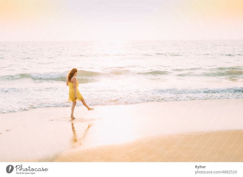 Goa, India. Young Caucasian Woman In Yellow Dress Walking Along Seashore In Summer Sunlight Arabian Sea Indian Ocean beautiful caucasian copy space distance