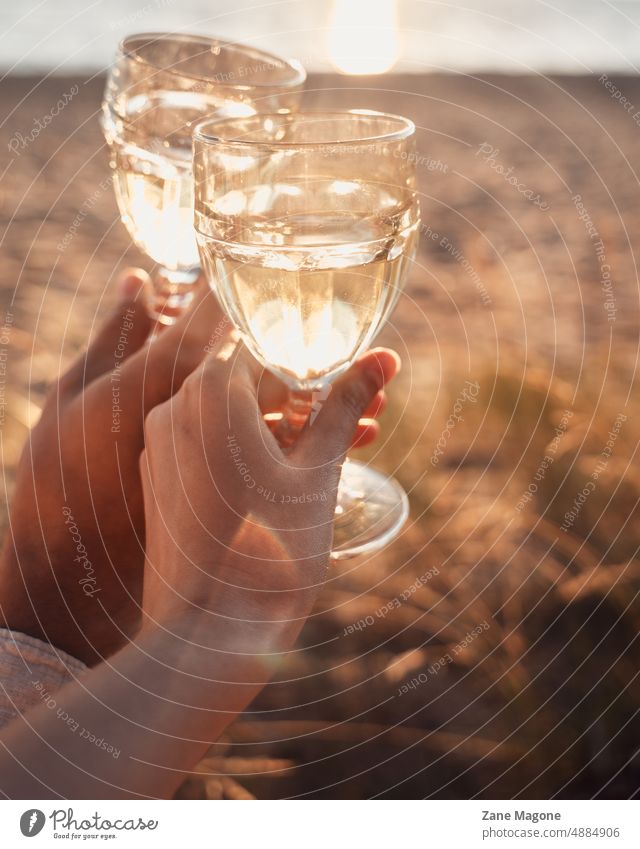 Couple holding glasses of drink at the bach, golden hours couple romantic picnic drinks wine wineglass Wine glass Champagne Alcoholic drinks romantic date beach