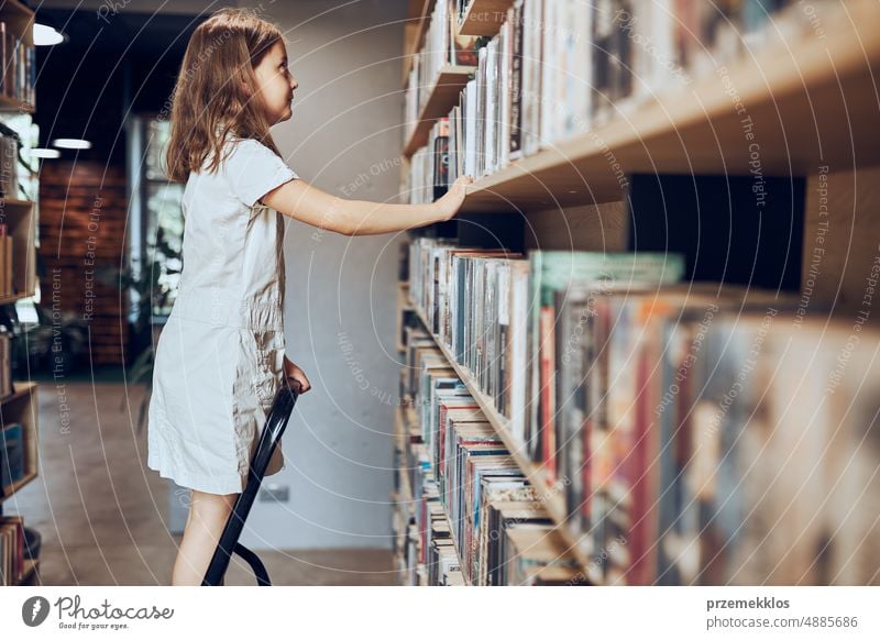 Schoolgirl looking at books on top bookshelf in school library. Smart girl selecting literature for reading. Benefits of everyday reading. Child curiosity. Back to school