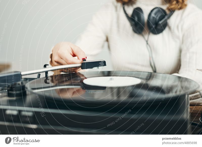 Young woman listening to music from vinyl record player. Playing music on turntable player. Female enjoying music from old record collection at home analog