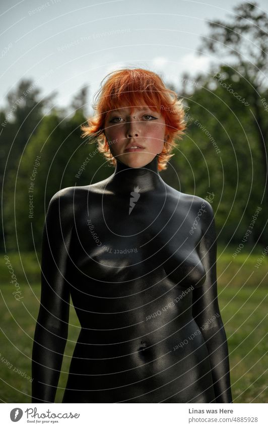 Having some fun with black paint and a red hair model. A gorgeous girl with her sexy curves almost all covered in body paint. Enjoying wild nature and hot summer. A portrait of an extraordinary woman.