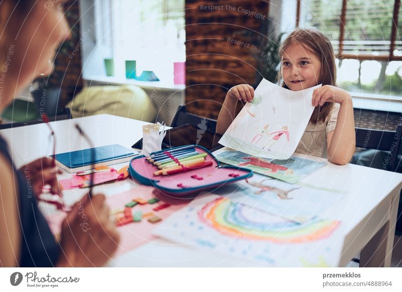 Girl presenting her artwork teacher. Woman assisting schoolgirl during classes at primary school. Child drawing picture sitting at desk in classroom. Learning at primary school. Back to school