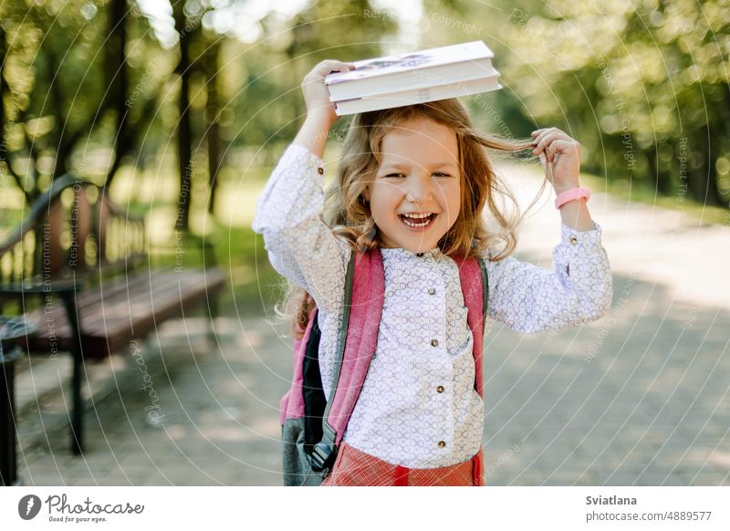 A charming little girl with a book on her head, on the first day at school or kindergarten. The concept of training and education child schoolgirl childhood