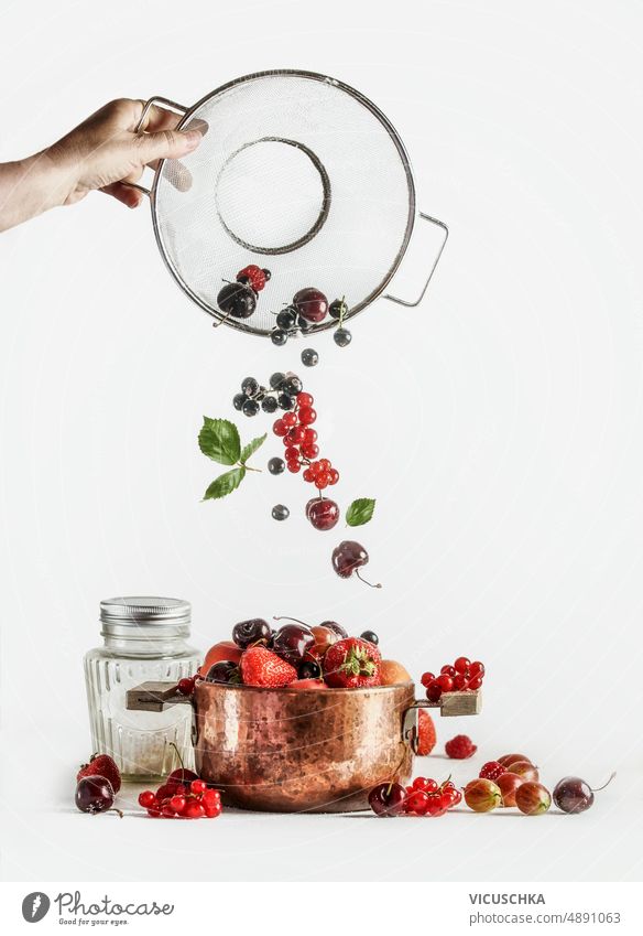 Women hand pours various berries out of a sieve in copper cooking pot. Jam preparation women pours out copper pot jam ingredients kitchen utensils front view