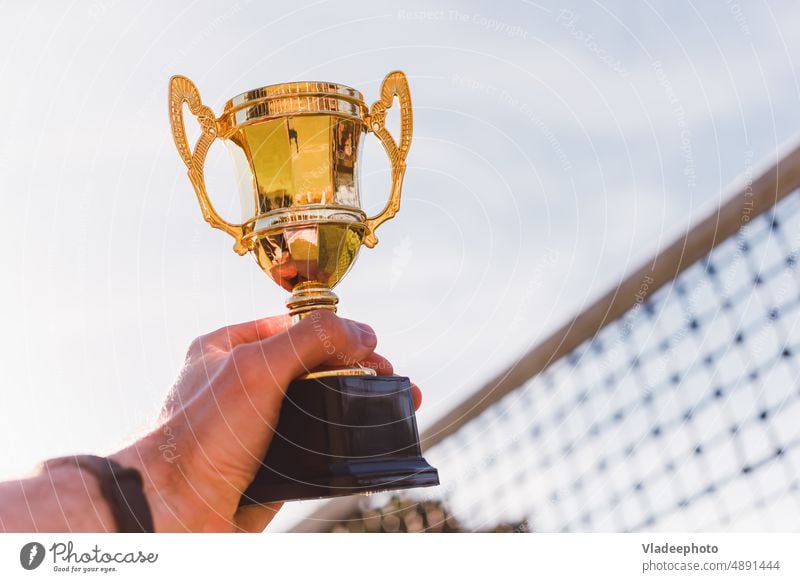 Golden cup in hand of sport competition winner with play net on background tennis golden prize grid volleyball badminton holds goblet court racket championship