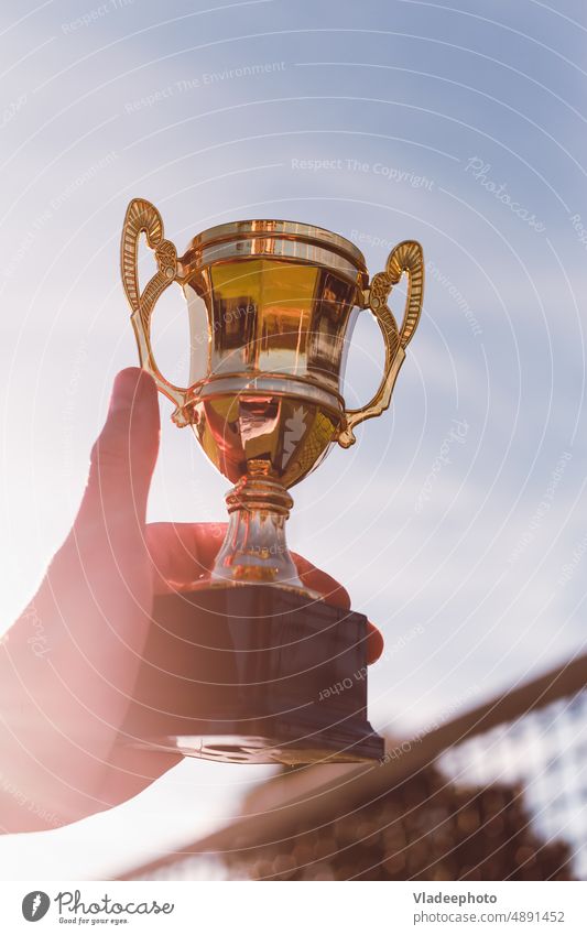 Golden cup in hand of sport competition winner with play net on background golden court racket ball championship goblet contest prize first success best victory