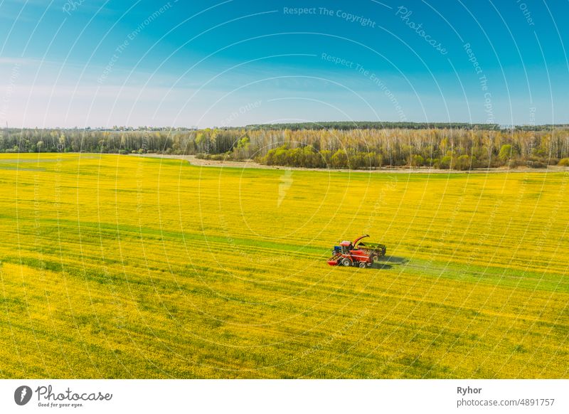 Aerial View Of Rural Landscape. Combine Harvester And Tractor Working Together In Field. Harvesting Of Oilseed In Spring Season. Agricultural Machines Collecting Blooming Rapeseeds Canola Colza. Elevated View