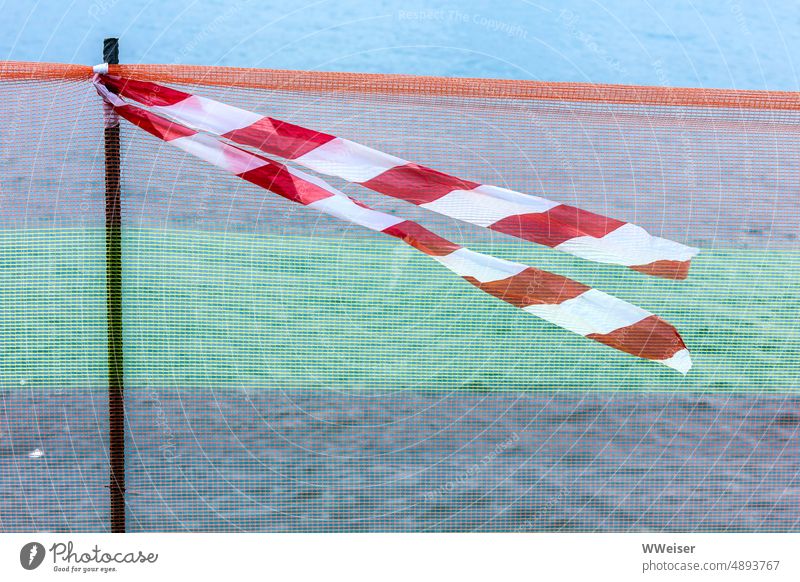 A piece of barrier tape flutters in the wind cordoned off Fence Band Judder windy forbidden Construction site repair Repair Promenade Dangerous peril