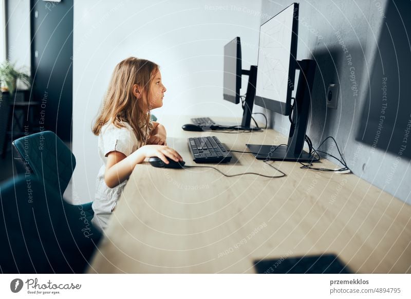 Absorbed schoolgirl learning to use technology in classroom at primary school. Child using computer on elementary computer science class. Back to school child