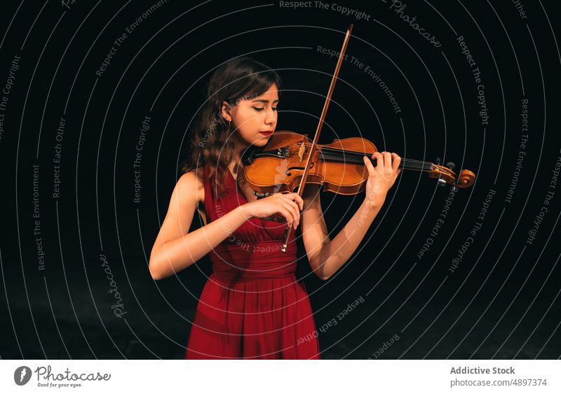 Female musician playing violin on stage woman concert perform theater dark female eyes closed instrument sound melody entertain practice elegant dress tune dim