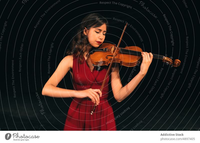 Female musician playing violin on stage woman concert perform theater dark female eyes closed instrument sound melody entertain practice elegant dress tune dim