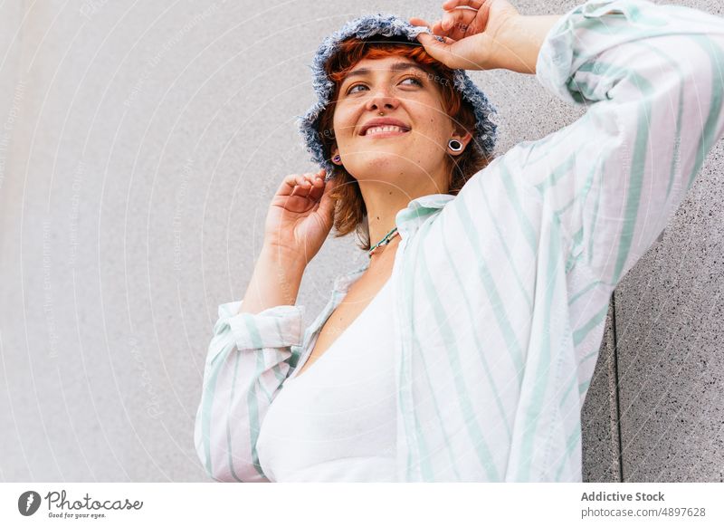 Smiling woman with hat near wall hobby pastime leisure street urban content smile activity enjoy cheerful wear casual building attractive summertime city female