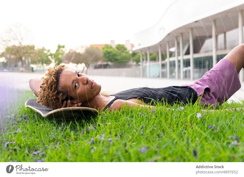 Black man lying on skateboard in city lawn skateboarder hobby sporty pastime leisure street rest building street style house confident male african american