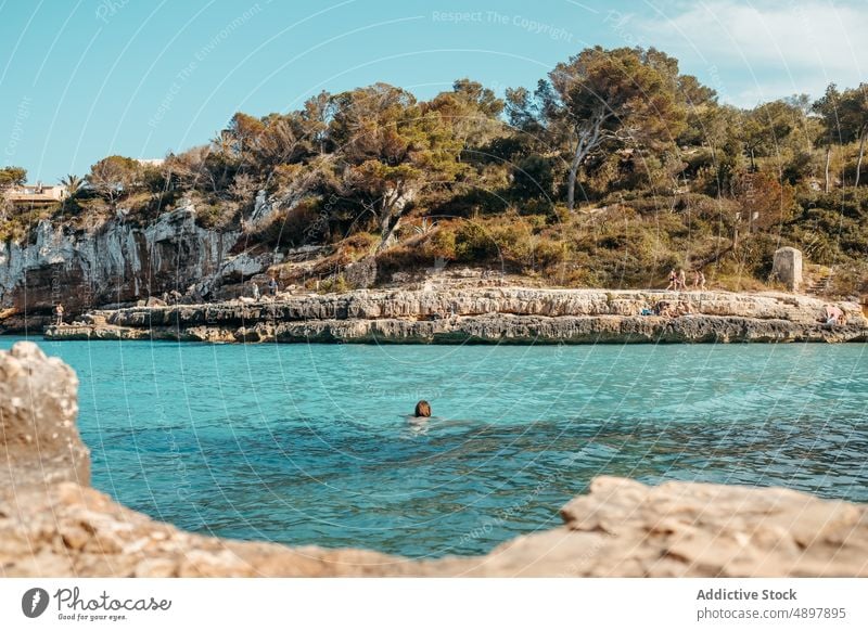 Anonymous lady swimming on rocky coast woman relax sea beach seashore admire holiday enjoy vacation recreation nature female young long hair wavy hair resort