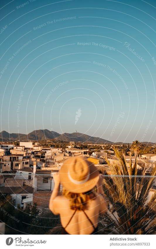 Anonymous feminine lady relaxing in rooftop at sunset woman vacation tourist admire style town holiday enjoy summer female young swimsuit straw hat hotel resort