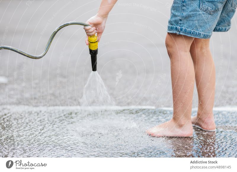 Boy Washing Road With Hose Water Spray Leg Hand Holding Wet Motion Low Section Lifestyle Standing Outside Self Service Activity Anonymous Unrecognizable Cropped