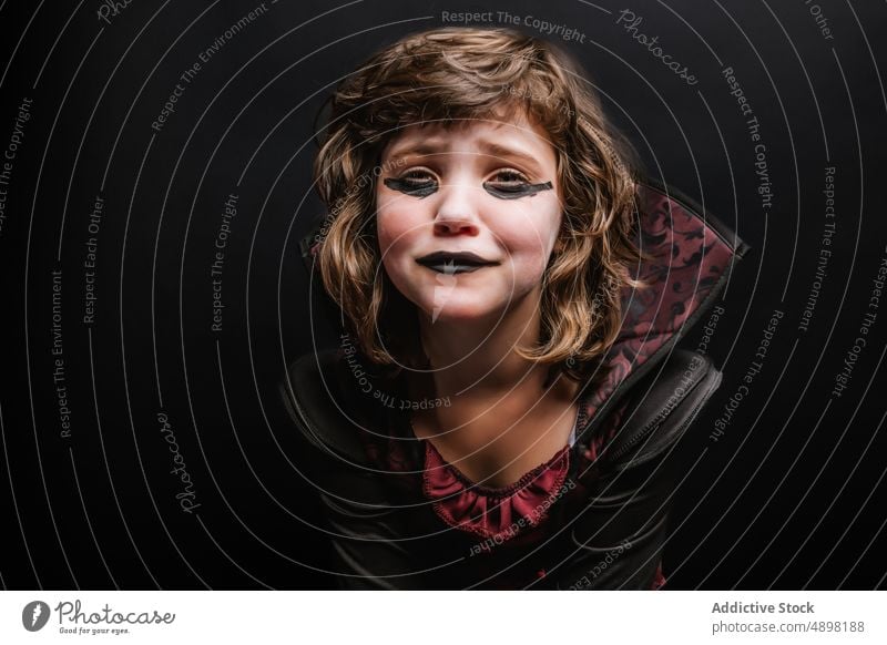 Sad little child in Halloween costume crying in dark studio halloween enchantress girl upset sad portrait witch carnival masquerade devil makeup kid curly hair