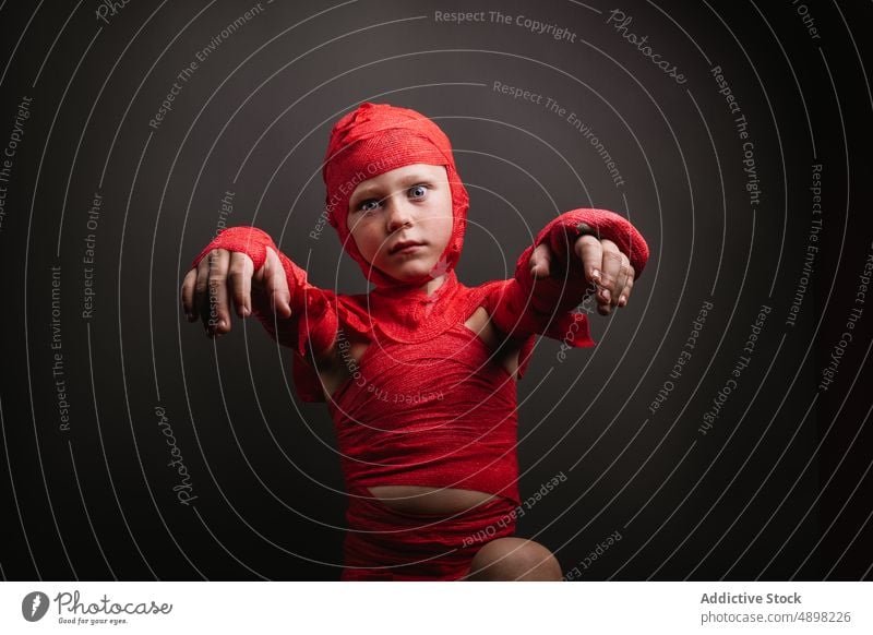 Cute little kid in mummy costume shouting and gesturing in grey studio child halloween boy scary portrait spooky reach out make face creepy adorable celebrate