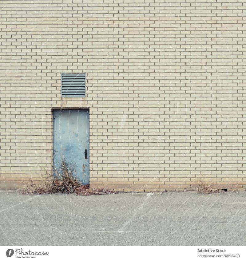 Brick building with door and ventilation abandoned brick wall shutter grass exterior street parking entrance construction structure shabby worn out daytime