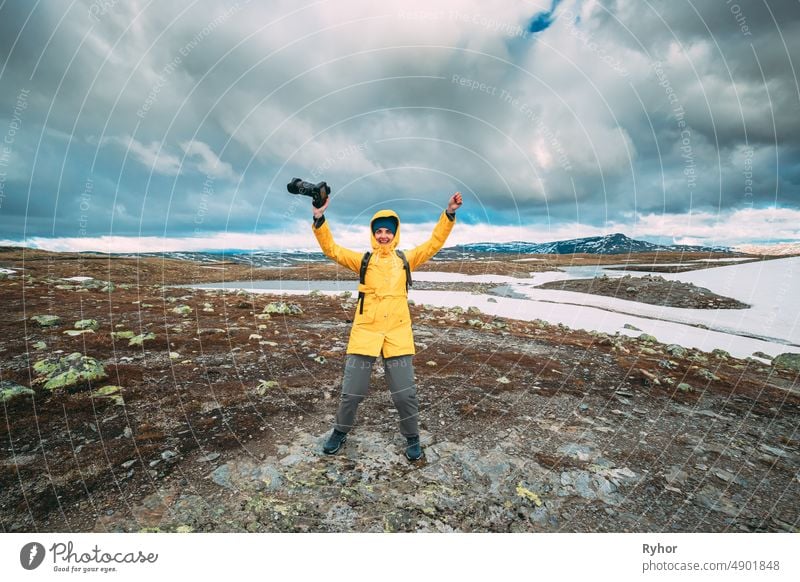 Aurlandsfjellet, Norway. Happy Young Woman Tourist Traveler Photographer With Camera Walking Near Aurlandsfjellet Scenic Route Road. Active Lifestyle In Norwegian Nature