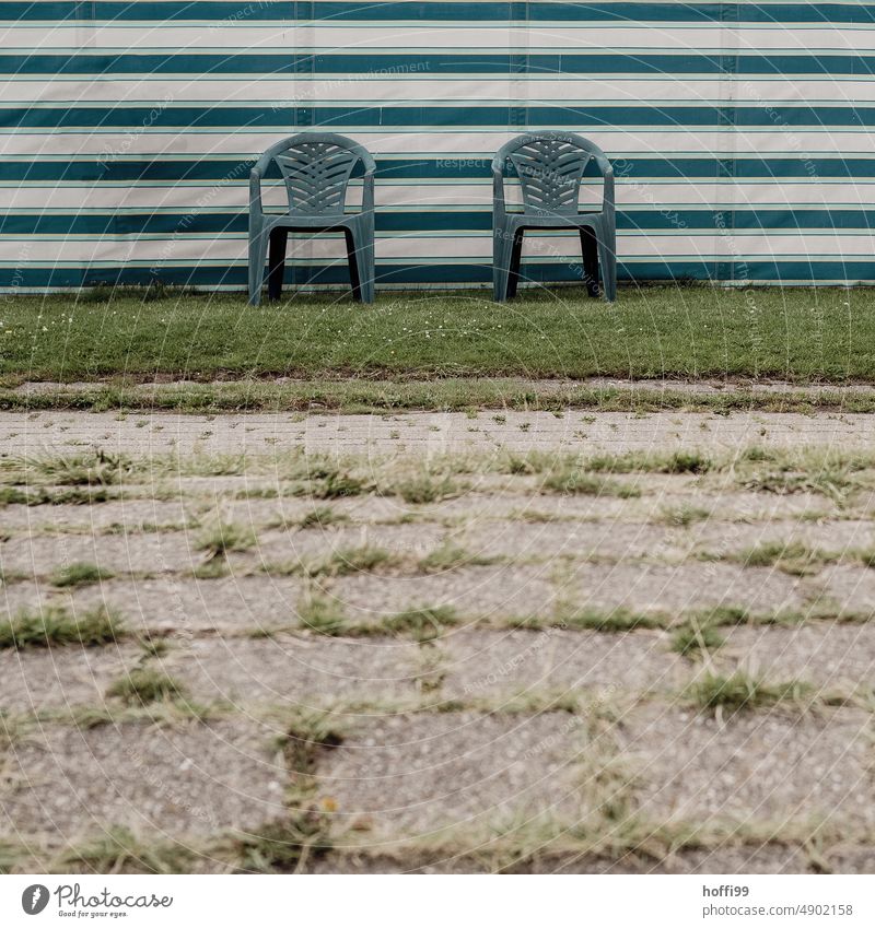 two blue plastic chairs on a strip of grass in front of a windbreak Plastic chair Plastic chairs Camping site wind deflector tarpaulin Lawn Stripe Relaxation