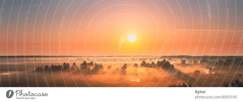 Amazing Sunrise Sunset Over Misty Landscape. Scenic View Of Foggy Morning Sky With Rising Sun Above Misty Forest And River. Early Summer Nature Of Eastern Europe. Panorama