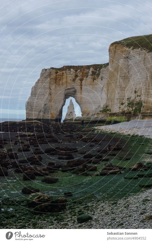 The Needle seen through the arch of the Manneporte cliff at the Alabaster coast on a cloudy summer day, Etretat, Normandy, France Étretat Rock Ocean Cliff