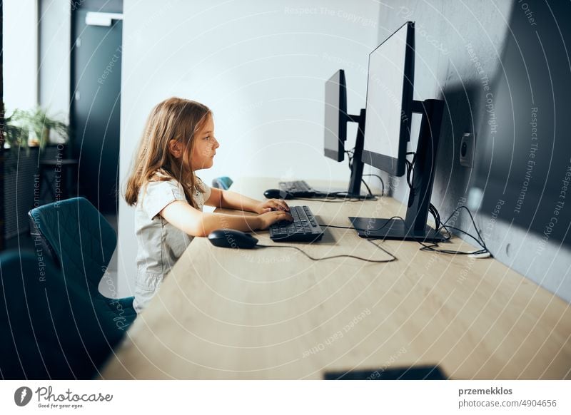 Bored schoolgirl sitting at desk in computer classroom at school. Child not interested learning to use computer. Boring class elementary primary technology