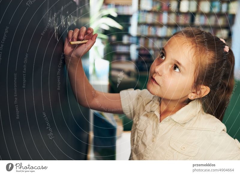 Little girl writing on blackboard. Smart student put solve on chalkboard. Back to school. Child having class. Schoolgirl learning at primary school back child