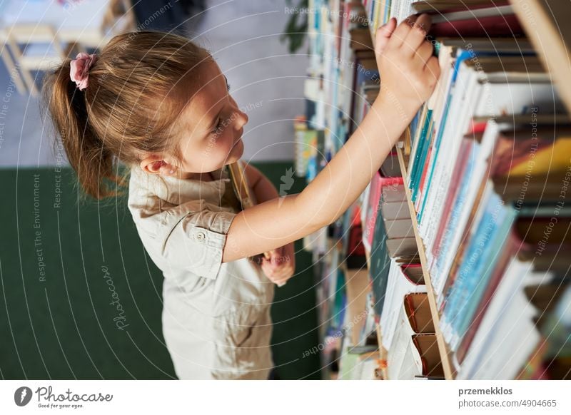 School girl looking at bookshelf in school library. Smart girl selecting literature for reading. Books on shelves in bookstore. Learning from books. Back to school. School education