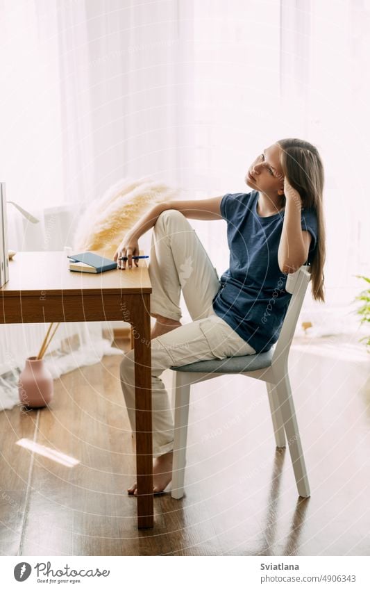 A high school student sits at home at her desk, takes a break before preparing for classes or exams, studies at home. The concept of training and education girl